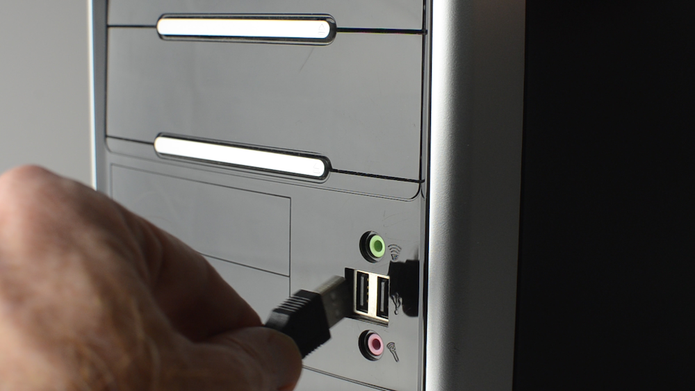 Shows a hand plugging a cord into the USB port of a computer to connect a USB scale